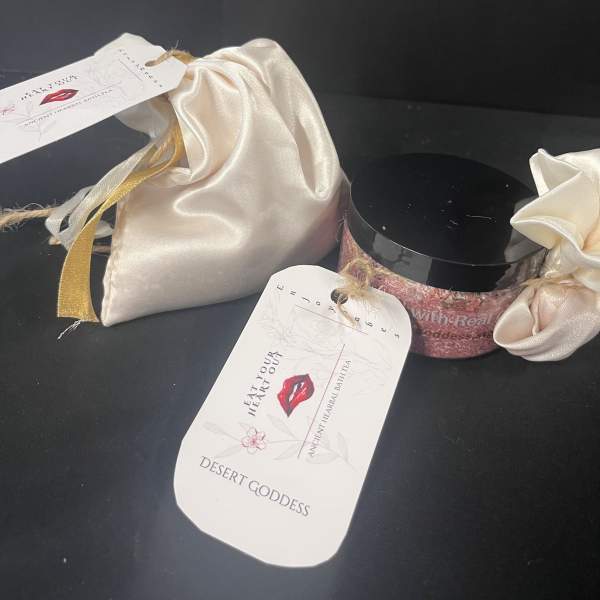 Two satin gift pouches and a pink jar with a black lid on a dark surface