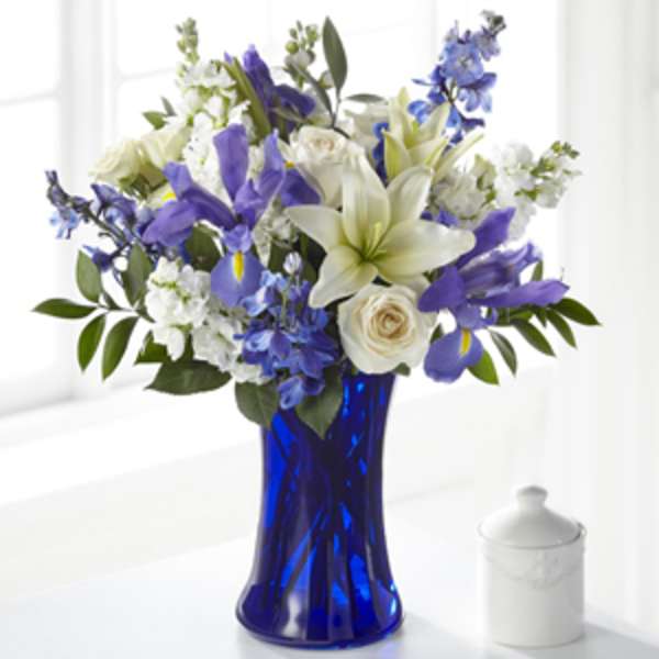 Blue and white bouquet with lilies, roses, irises, and delphinium in a cobalt glass vase