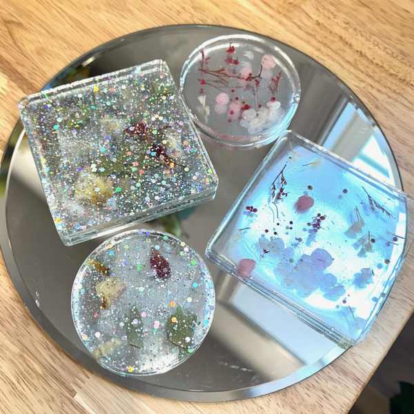 Four resin coasters with embedded dried flowers and glitter on a round tray