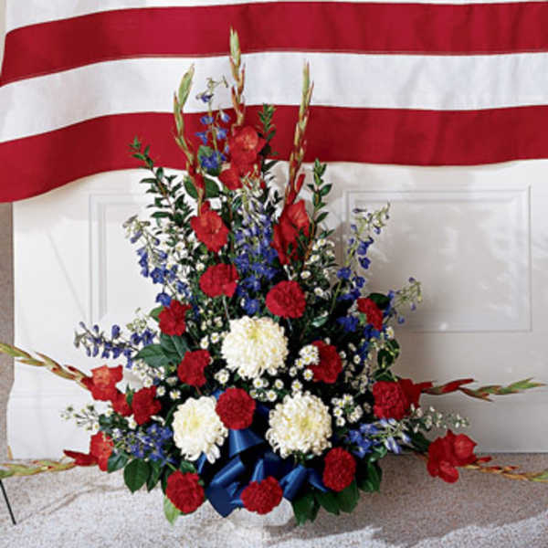Red, white, and blue floral standing spray in front of a flag