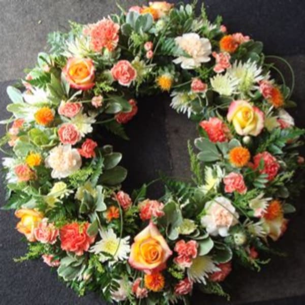 Circular floral wreath with mixed roses, carnations, and white daisy-like blooms