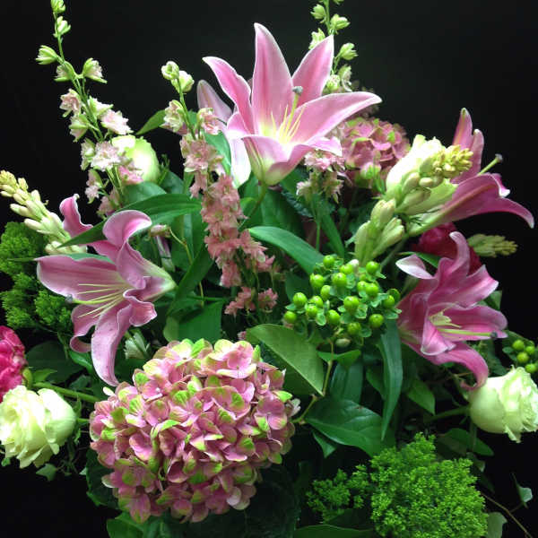 Tall arrangement of pink lilies and hydrangea with white blooms in a clear glass vase