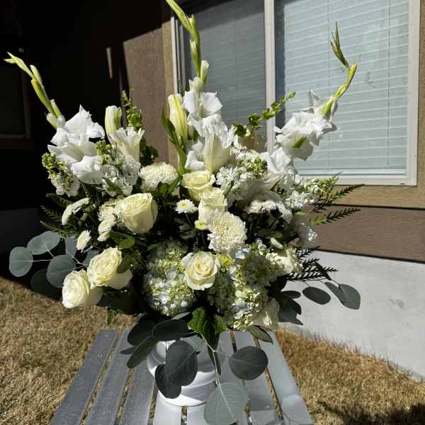 White floral arrangement in a white vase with roses and tall gladiolus