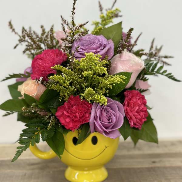 Mixed pink and purple bouquet in a yellow smiley-face mug