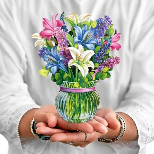Person holding a small vase of colorful lilies and lilacs