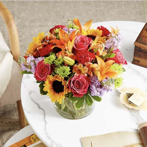 Mixed bouquet of roses, sunflowers, lilies, and carnations in a glass vase