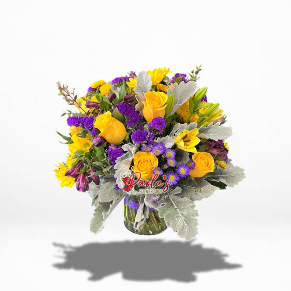Bouquet of yellow roses, purple flowers, and lilies in a glass vase