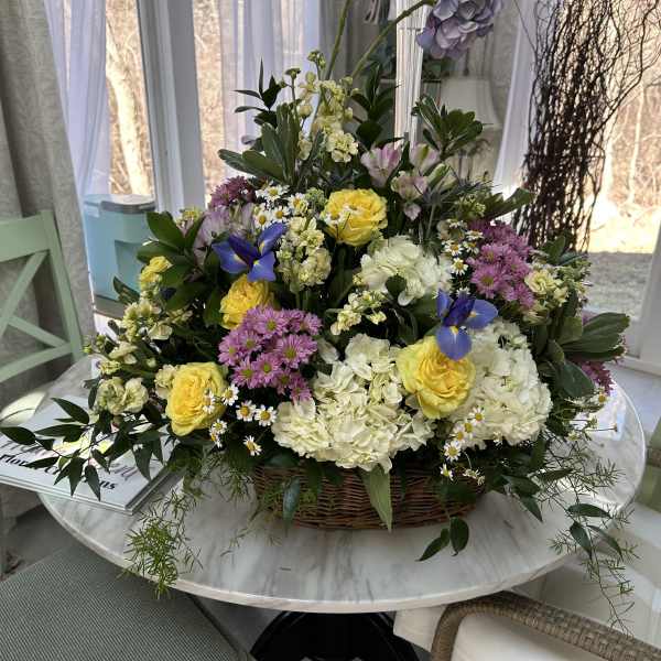 Basket arrangement of yellow roses, white hydrangeas, and purple flowers