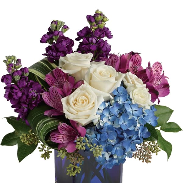 Bouquet of white roses, purple flowers, and blue hydrangea in a square vase