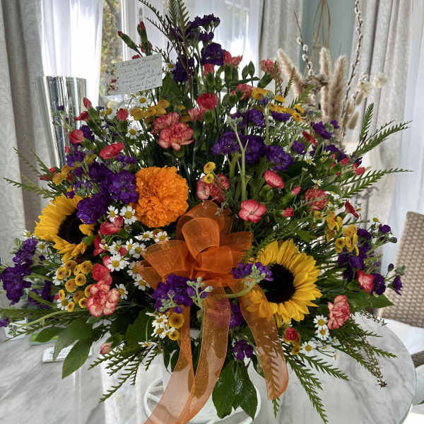 Large mixed bouquet with sunflowers, purple blooms, and an orange ribbon