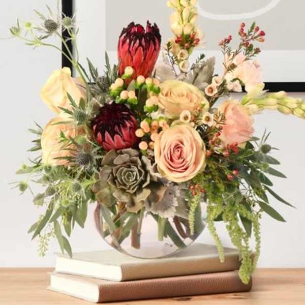 Mixed bouquet with pale roses and red protea in a round vase