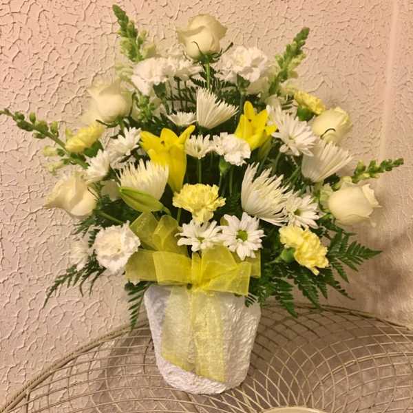 White and yellow floral arrangement in a white vase with a yellow ribbon