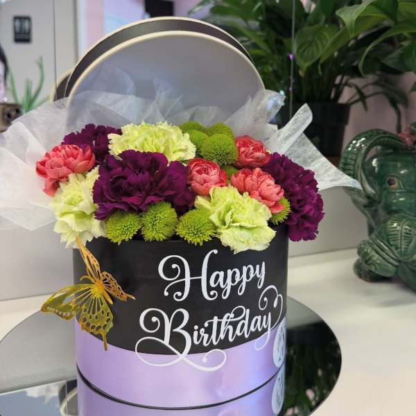 Birthday flower arrangement in a round gift box with pink, purple, and green blooms