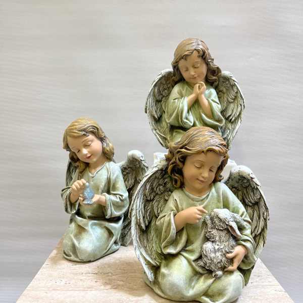 Three angel figurines in pale green robes sit on a stone base.