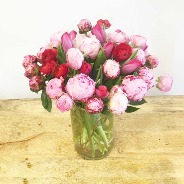 Pink and red tulips and peonies in a clear glass vase