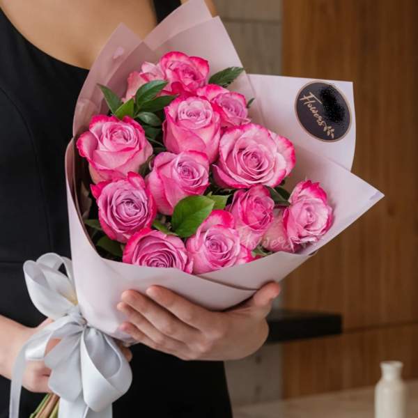 Bouquet of pink roses wrapped in pale paper with a white ribbon