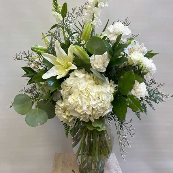 White floral arrangement in a clear glass vase with lilies and hydrangea