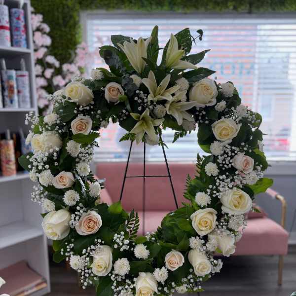 Standing wreath of white lilies, ivory roses, and small white blooms on a metal easel