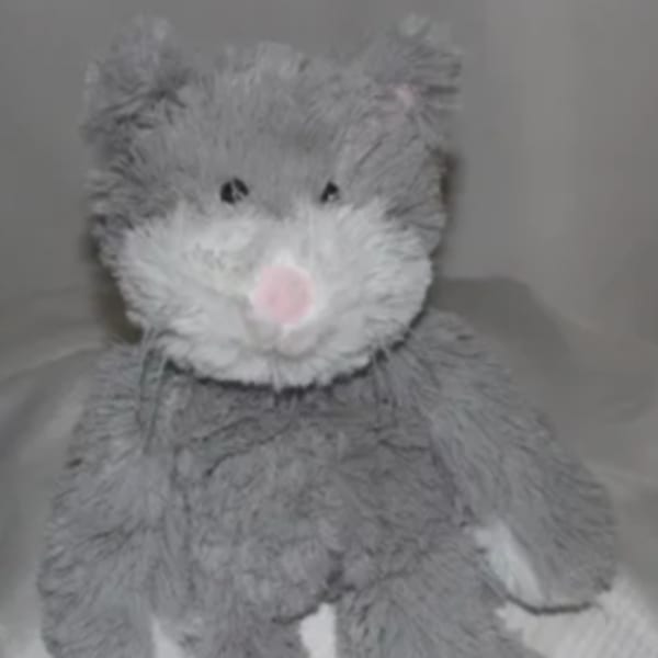 Gray plush teddy bear with a pink nose sitting on a bed