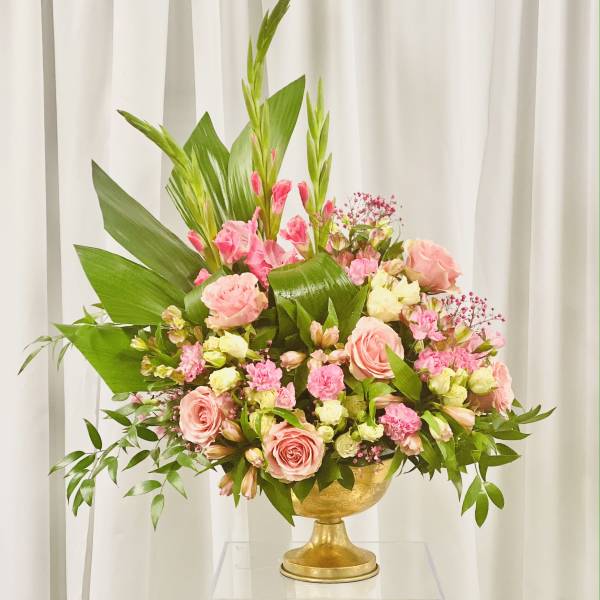 Pink roses and mixed blooms arranged in a gold pedestal vase