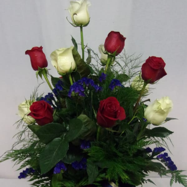 Red and white roses arranged in a glass vase with blue filler flowers.