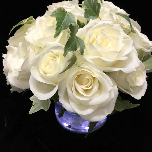Low arrangement of white roses in a round glass vase with soft interior lights.