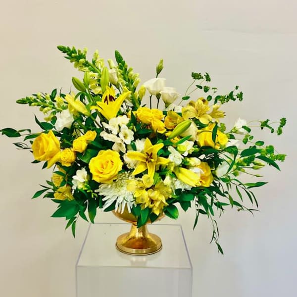 Yellow and white floral arrangement in a gold pedestal vase
