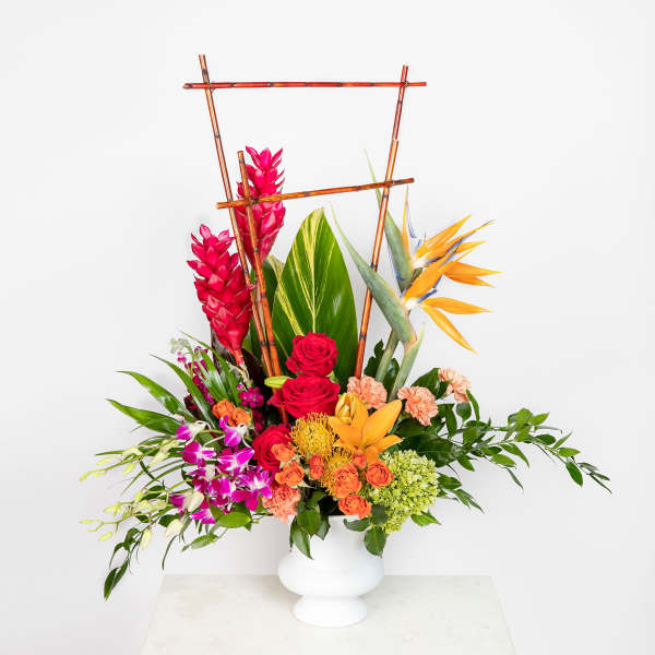 Tall tropical arrangement with orange lilies and birds of paradise, red roses, and purple orchids in a white vase