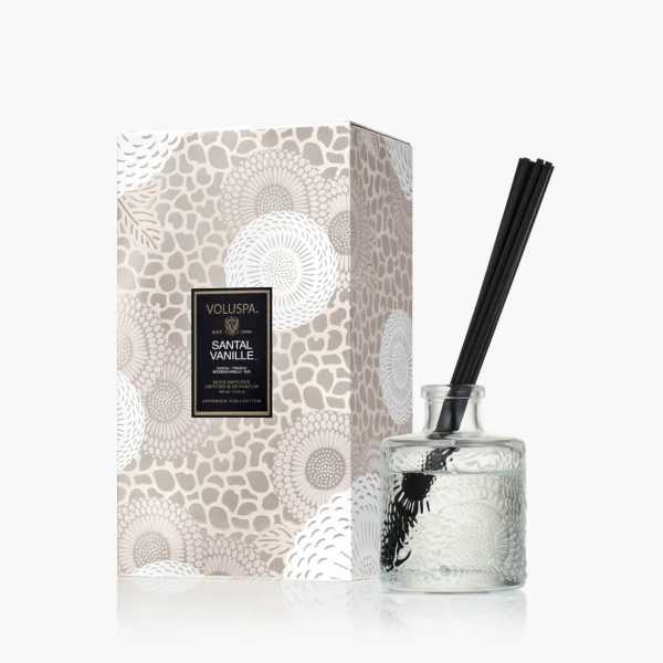 Glass reed diffuser with black reeds beside a patterned box