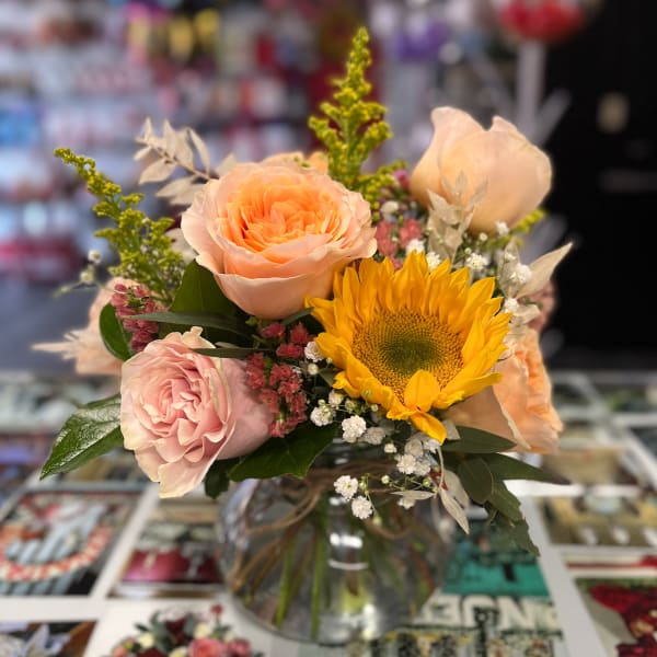 Bouquet of peach roses and a yellow sunflower in a glass vase