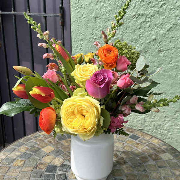 Bright arrangement of yellow roses, pink blooms, and orange tulips in a white vase on a mosaic table