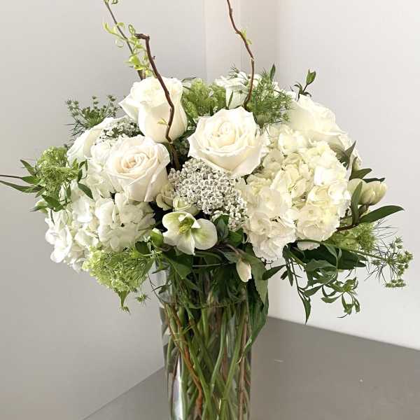 White roses and hydrangeas in a clear glass vase with greenery