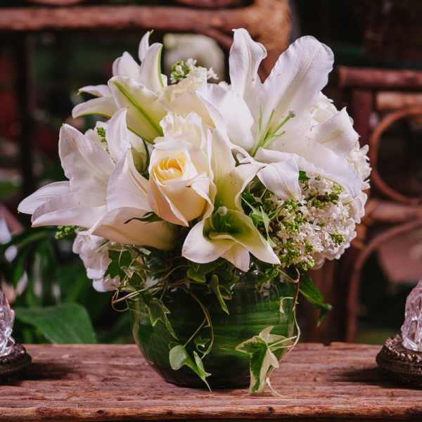 White lilies and roses arranged in a green glass vase