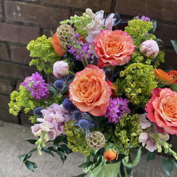 Bouquet of coral roses, purple blooms, and green filler flowers