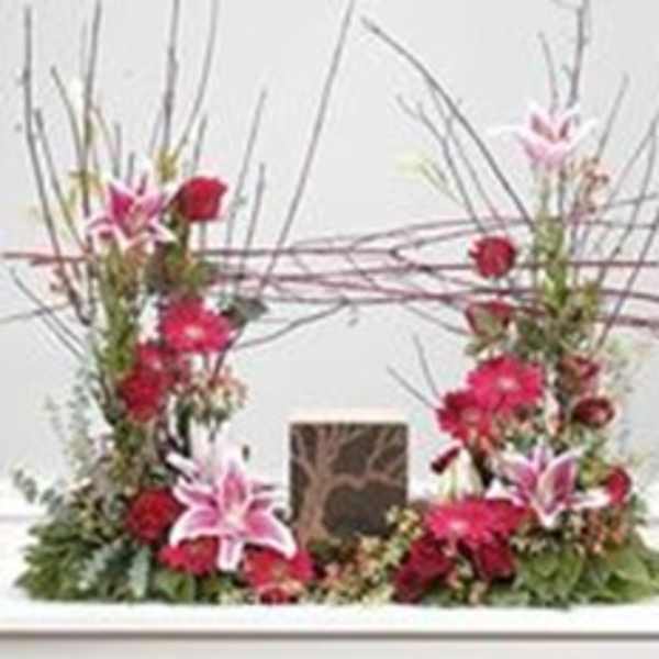 Tall floral arrangement with pink lilies and red flowers around a central vase