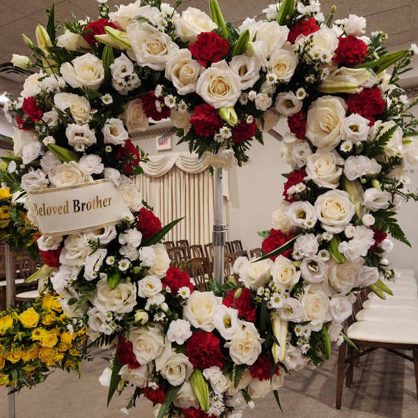 Large heart-shaped floral wreath with white and red flowers on a stand