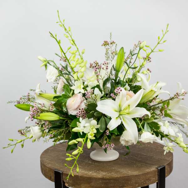 White lily and orchid arrangement in a white pedestal vase