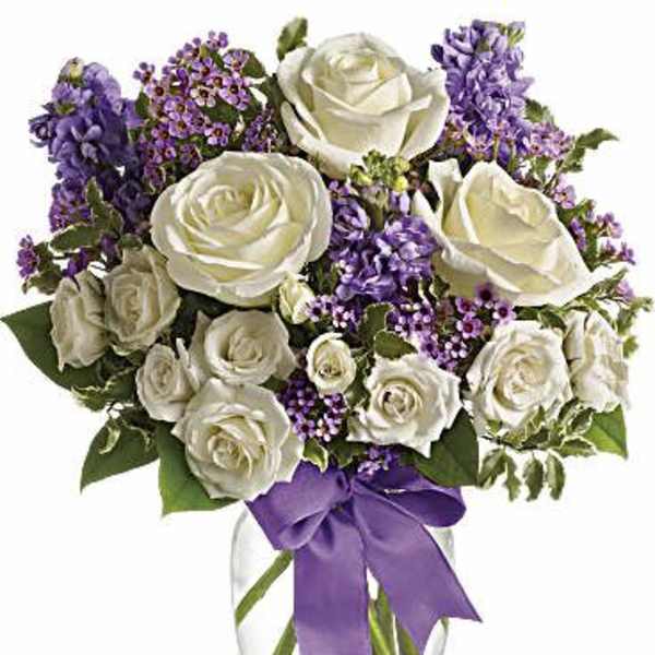 White roses and purple flowers in a clear glass vase with a purple ribbon