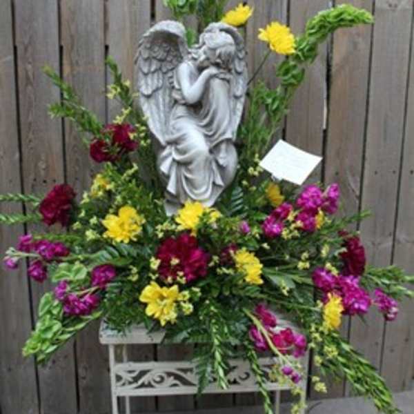 Floral arrangement with an angel statue and bright yellow, magenta, and red flowers