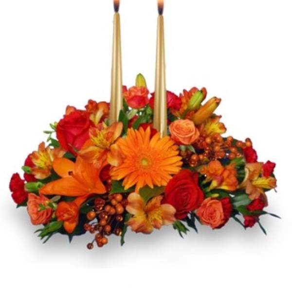 Low centerpiece of orange and red flowers with two tall gold taper candles in the center