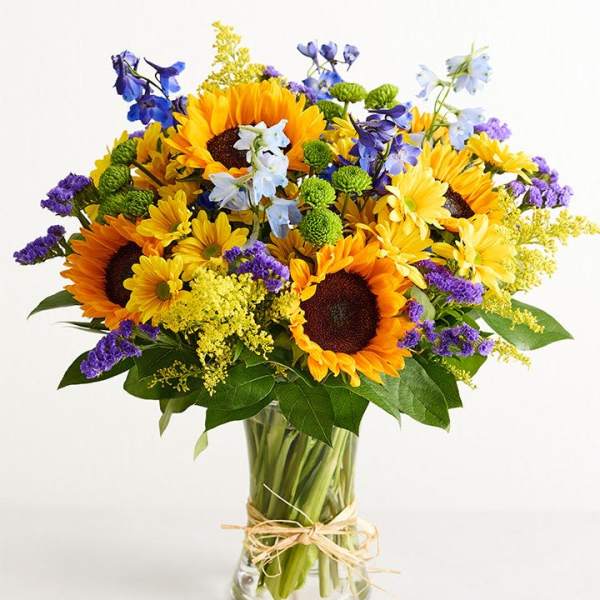 Bouquet of sunflowers, blue flowers, and purple filler in a glass vase