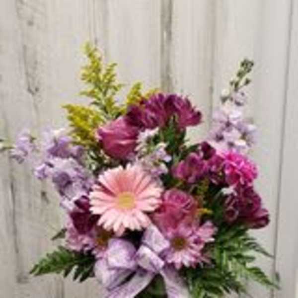 Mixed pink and purple flowers in a glass vase with a lavender ribbon