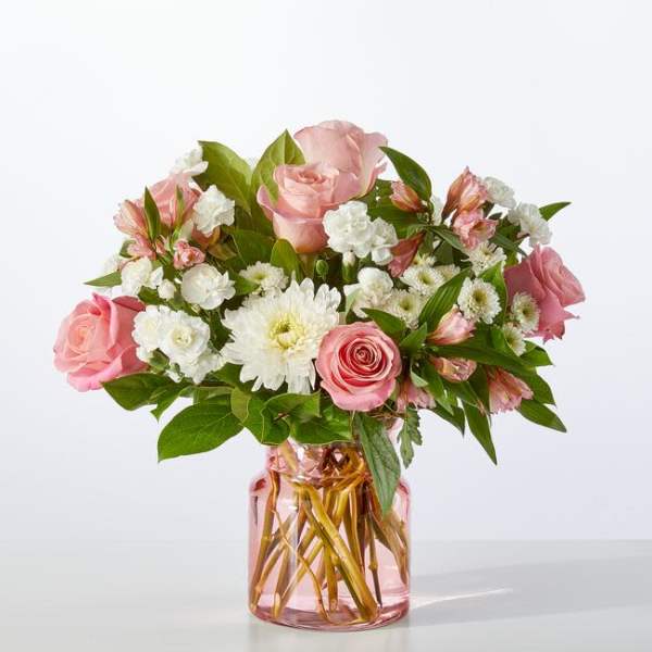 Pink roses and white daisies arranged in a pink glass vase