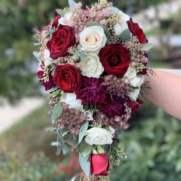 Handheld bouquet of red and white roses with small pink filler flowers