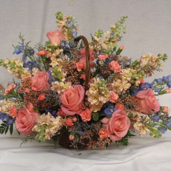 Basket arrangement of pink roses and blue flowers