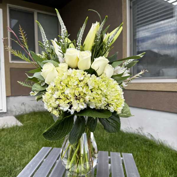 White roses and pale green hydrangea in a clear glass vase