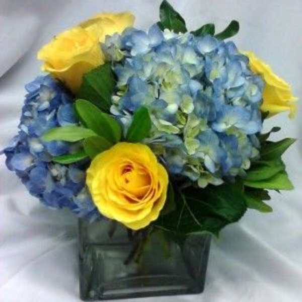 Blue hydrangeas and yellow roses in a square glass vase