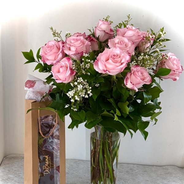 Pink roses in a clear glass vase beside a chocolate gift bag