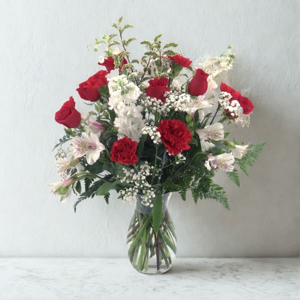 Bouquet of red roses, white flowers, and pink-striped blooms in a glass vase