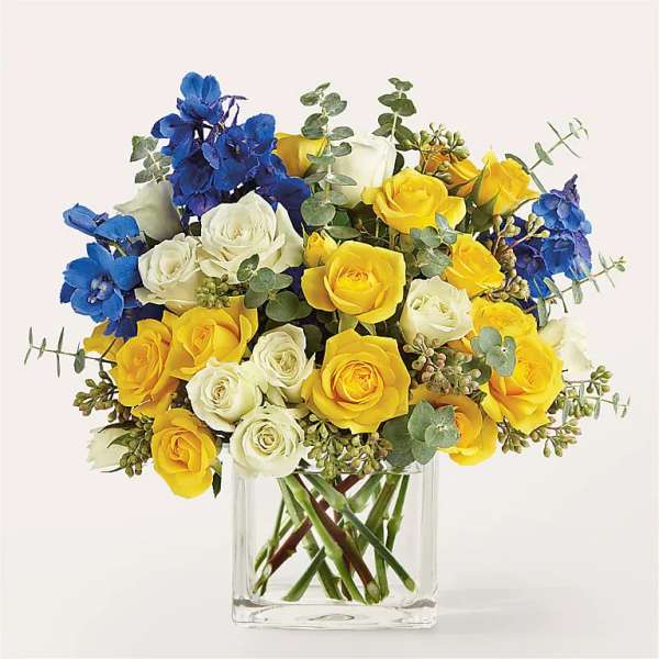 Bouquet of yellow and white roses with blue flowers in a clear glass vase